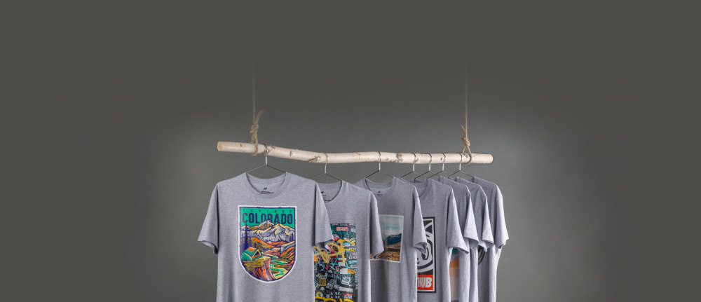 Gray t-shirts with colorful designs on a wooden rack against a dark background